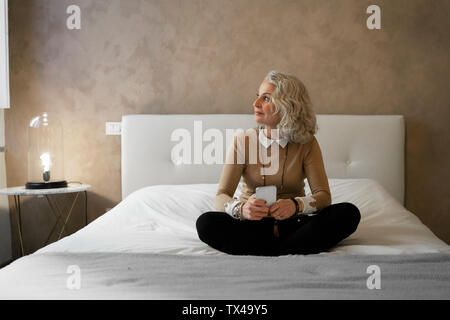 Coppia imprenditrice seduta sul letto con telefono mobile guardando fuori della finestra Foto Stock