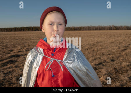 Ritratto di ragazzo vestito come supereroe nel paesaggio di steppa soffiando una gomma da masticare bubble Foto Stock