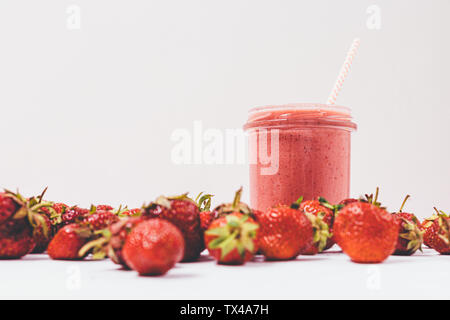 Vista anteriore frullato fragole in un barattolo di vetro con paglia accanto ai frutti di bosco freschi su sfondo bianco. Foto Stock
