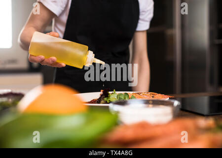 Close-up della donna per la cottura in cucina versando olio d'oliva in un piatto di portata Foto Stock