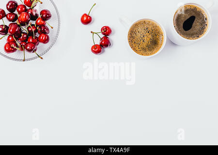Piatto telaio laici di caffè e bacche di snack sani su sfondo bianco con copia spazio. Vista dall'alto due tazze di caffè espresso e una ciotola di ciliegie. Foto Stock