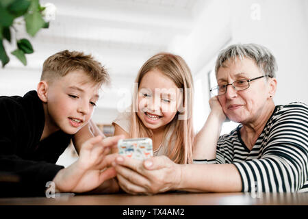 Nonna felice e i nipoti tramite telefono cellulare a casa Foto Stock