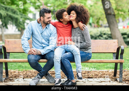 Famiglia seduta su una panchina nel parco, figlio di baciare la madre Foto Stock