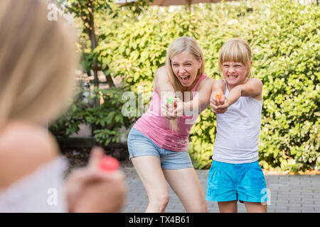 Madre e due ragazze di spruzzi di acqua con pistole in giardino Foto Stock