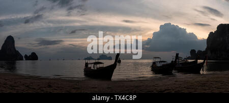 Thailandia, Krabi, Railay Beach, baia con coda lunga barche galleggiante sull'acqua al tramonto Foto Stock