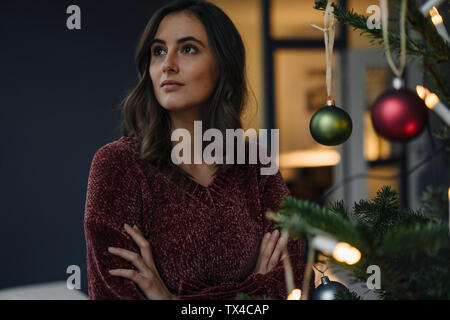 Giovane donna ad albero di Natale decorato che guarda lontano Foto Stock