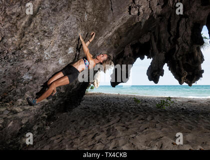 Thailandia, Krabi, Lao liang island, donna bouldering nella parete di roccia in spiaggia Foto Stock