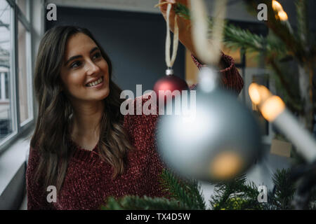 Sorridente giovane donna decorare albero di Natale Foto Stock