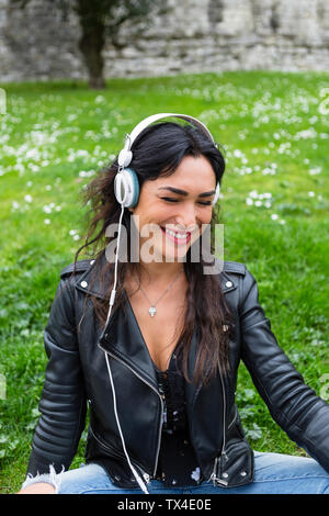 Ritratto di giovane donna con cuffie bianche, vestita di nero giacca di pelle Foto Stock