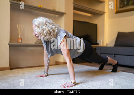 Donna matura facendo esercizi Yoga nella stanza vivente Foto Stock