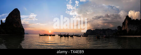 Thailandia, Krabi, Railay Beach, baia con coda lunga barche galleggiante sull'acqua al tramonto Foto Stock