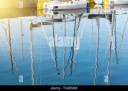 Piccole barche a vela in un marina con piloni riflettendo sul blu superficie di acqua Foto Stock