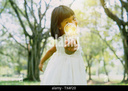 Risparmiare energia e concetto di mondo, giovane ragazza con lampadina in posizione di parcheggio Foto Stock