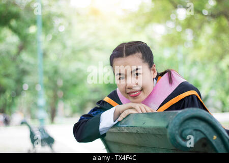 Felice e contento graduato studente asiatico ubicazione sul braccio shair nel parco, congratulazioni, laureato istruzione successo, il concetto di istruzione e finito di learni Foto Stock