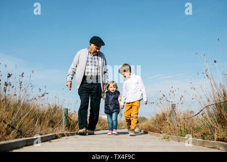 Nonno passeggiando con i suoi nipoti mano nella mano sul lungomare Foto Stock