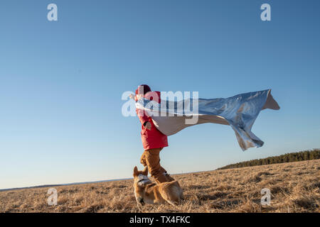 Ragazzo vestito come supereroe in esecuzione con il cane nel paesaggio di steppa Foto Stock