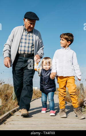 Nonno passeggiando con i suoi nipoti mano nella mano sul lungomare Foto Stock