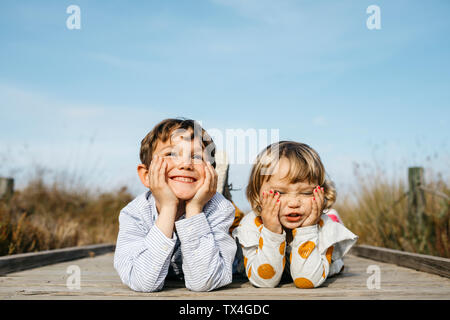 Ritratto di ragazzo e la sua sorellina affiancati sul Boardwalk tirando funny faces Foto Stock