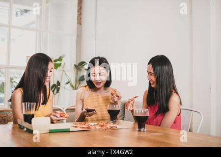 Il gruppo di donne asiatiche tanager mangiare la pizza e parlare di divertente, cibo parte a casa Foto Stock
