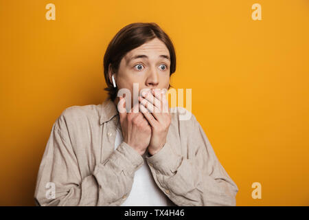 Scioccato bel Uomo in camicia che copre la bocca mentre guarda lontano su sfondo giallo Foto Stock