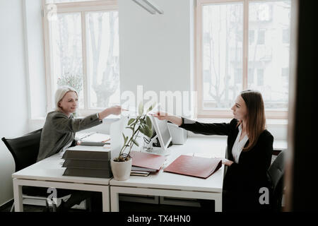 Due giovani donne che lavorano alla scrivania in ufficio consegna carta Foto Stock