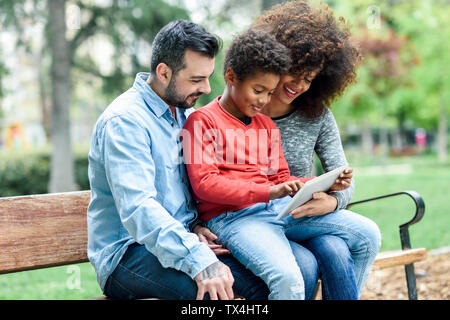 Famiglia seduta su una panchina nel parco, utilizzando tavoletta digitale Foto Stock