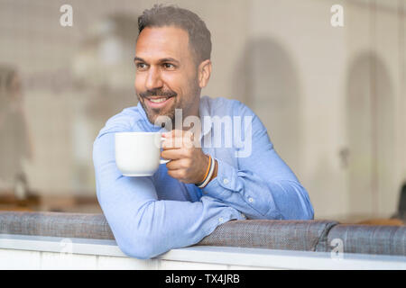 Imprenditore sorridente con tazza di caffè guardando fuori della finestra Foto Stock