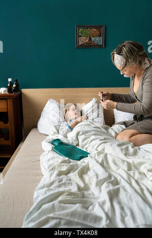 Madre tenendo la temperatura del malato figlia giacente a letto Foto Stock