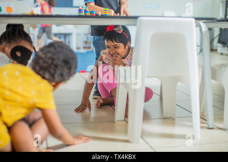 Allegro ragazze giocare sotto la tabella in una scuola materna Foto Stock