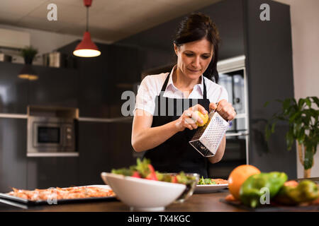 La donna la cottura in cucina versando il limone grattugiato su un piatto di portata Foto Stock