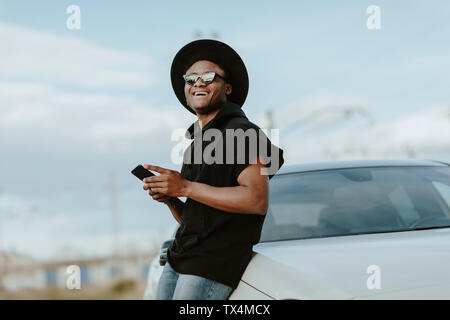 Ritratto di un giovane uomo di invio di un messaggio di posta elettronica con il telefono, ridendo Foto Stock