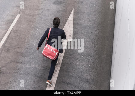 Vista posteriore di imprenditore in esecuzione su strada con segno di freccia Foto Stock