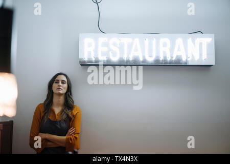 Grave giovane donna appoggiata contro una parete sotto il ristorante luce al neon Foto Stock