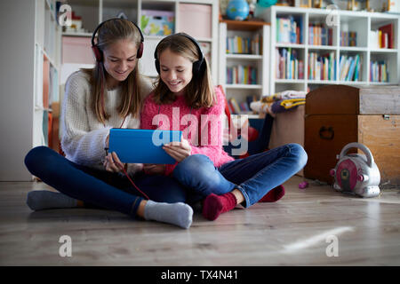 I fratelli a giocare a casa con loro compresse digitale, seduti a terra Foto Stock