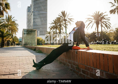 Giovane donna seduta su una parete, godendo di luce solare Foto Stock