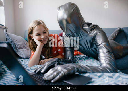 Uomo in morphsuit e ragazza distesa sul divano di casa utilizzando laptop Foto Stock