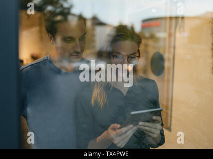 Giovane uomo e donna tablet condivisione dietro il vetro di finestra Foto Stock