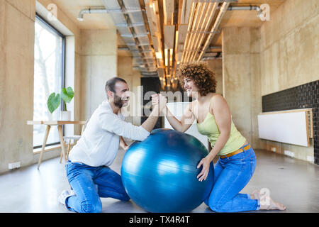 Felice l'uomo e donna wrestling braccio sulla sfera di fitness in ufficio moderno Foto Stock