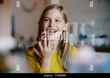 Felice ragazza seduta al tavolo della cucina a casa giocando con lamponi Foto Stock