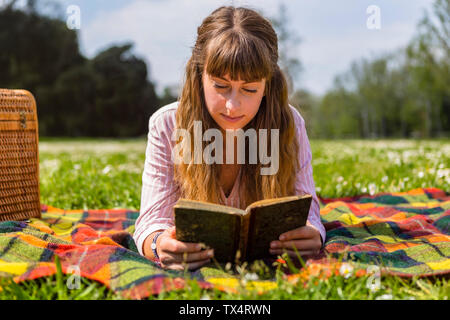 Giovane donna sdraiata su una coperta picnic, la lettura di un libro in un parco Foto Stock