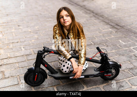 Ritratto di una ragazza che indossa golden sequin jacket inginocchiati su piegato E-scooter Foto Stock