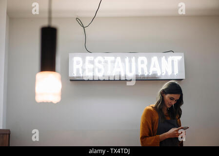 Giovane donna tramite telefono cellulare sotto il ristorante luce al neon Foto Stock