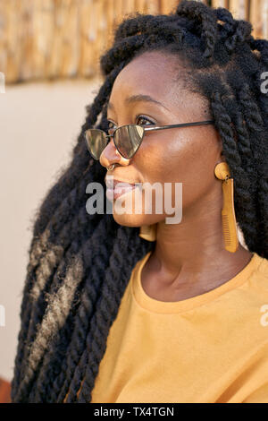 Ritratto di giovane donna con piercing per il naso, occhiali da sole e dreadlocks Foto Stock