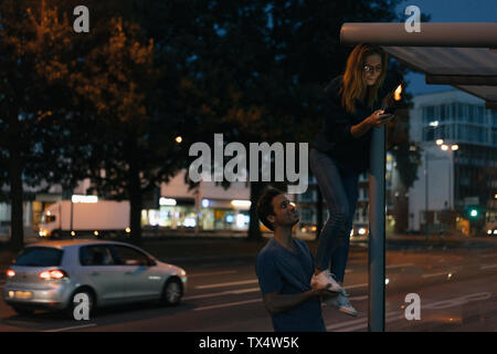 Giovane uomo dando fidanzata con un telefono cellulare di una gamba nella città di notte Foto Stock