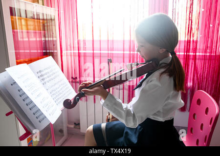 Ragazza seduta alla finestra a casa suona il violino Foto Stock