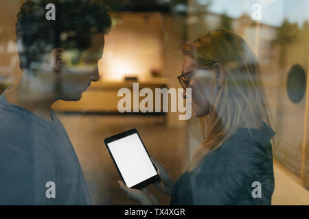 Giovane uomo e donna tablet condivisione dietro il vetro di finestra Foto Stock