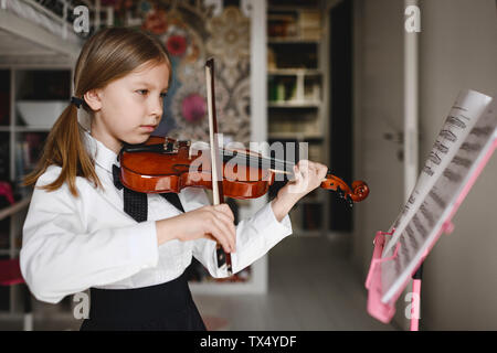 Ragazza suona il violino guardando il music stand a casa Foto Stock