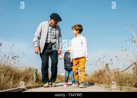 Nonno passeggiando con i suoi nipoti mano nella mano sul lungomare Foto Stock