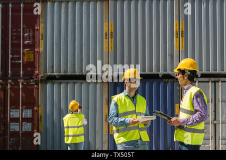 Lavoratori parlando vicino a pila di contenitori di carico sul sito industriale Foto Stock