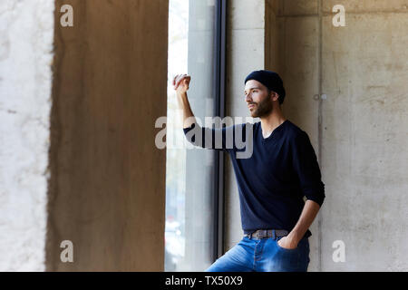 Giovane uomo che indossa beanie guardando fuori della finestra Foto Stock